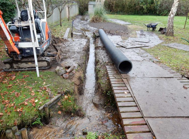Garden Drainage and Brook Management Worplesdon, Guildford, Surrey - An existing brook had become over grown and blocked with vegetation and silt build up. Brook was cleared, re-ditched, a new under ground pipe installed, surrounding banks and lawns re-turfed and finally construction of a new Oak sleeper bridge to replace the old one. Garden Drainage - MDB Landscapes