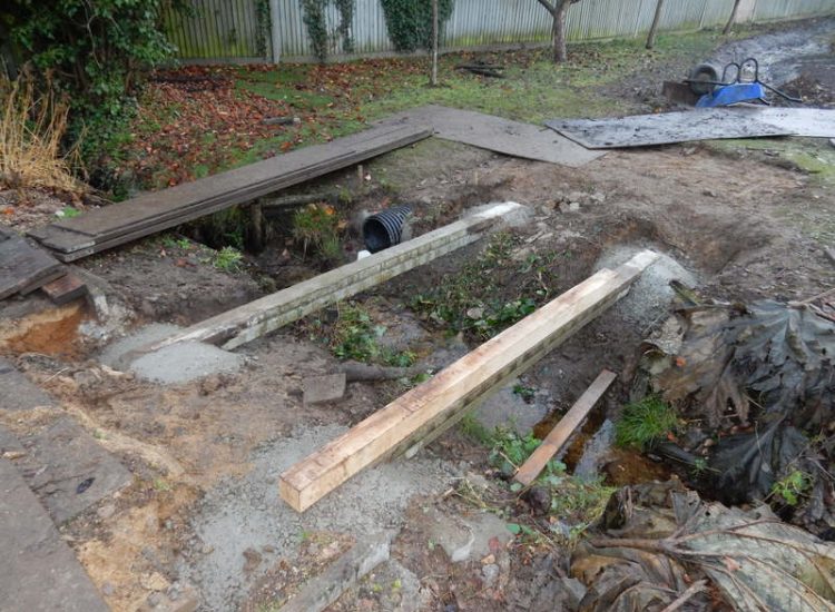 Garden Drainage and Brook Management Worplesdon, Guildford, Surrey - An existing brook had become over grown and blocked with vegetation and silt build up. Brook was cleared, re-ditched, a new under ground pipe installed, surrounding banks and lawns re-turfed and finally construction of a new Oak sleeper bridge to replace the old one. Garden Drainage - MDB Landscapes