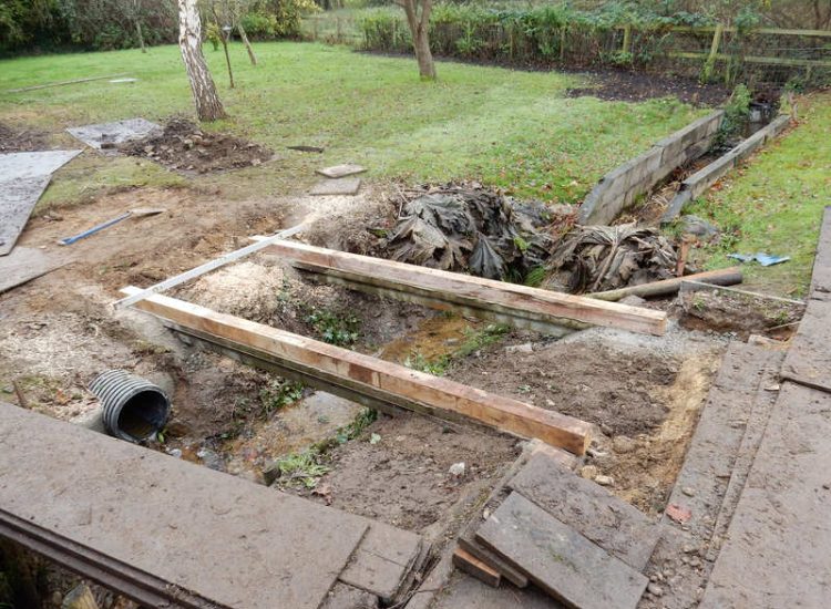 Garden Drainage and Brook Management Worplesdon, Guildford, Surrey - An existing brook had become over grown and blocked with vegetation and silt build up. Brook was cleared, re-ditched, a new under ground pipe installed, surrounding banks and lawns re-turfed and finally construction of a new Oak sleeper bridge to replace the old one. Garden Drainage - MDB Landscapes