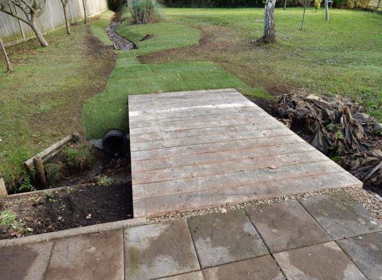 Garden Drainage and Brook Management Worplesdon, Guildford, Surrey - An existing brook had become over grown and blocked with vegetation and silt build up. Brook was cleared, re-ditched, a new under ground pipe installed, surrounding banks and lawns re-turfed and finally construction of a new Oak sleeper bridge to replace the old one. Garden Drainage - MDB Landscapes