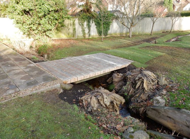 Garden Drainage and Brook Management Worplesdon, Guildford, Surrey - An existing brook had become over grown and blocked with vegetation and silt build up. Brook was cleared, re-ditched, a new under ground pipe installed, surrounding banks and lawns re-turfed and finally construction of a new Oak sleeper bridge to replace the old one. Garden Drainage - MDB Landscapes
