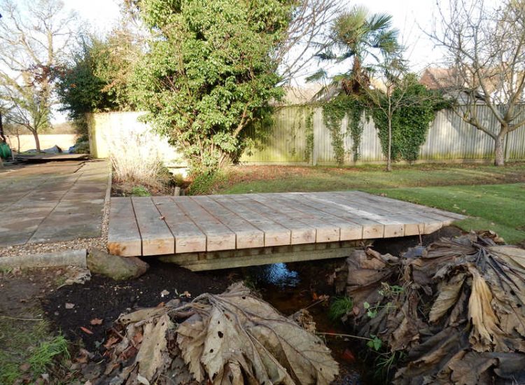 Garden Drainage and Brook Management Worplesdon, Guildford, Surrey - An existing brook had become over grown and blocked with vegetation and silt build up. Brook was cleared, re-ditched, a new under ground pipe installed, surrounding banks and lawns re-turfed and finally construction of a new Oak sleeper bridge to replace the old one. Garden Drainage - MDB Landscapes