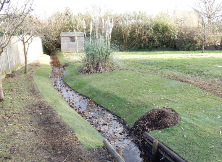 Garden Drainage and Brook Management Worplesdon, Guildford, Surrey - An existing brook had become over grown and blocked with vegetation and silt build up. Brook was cleared, re-ditched, a new under ground pipe installed, surrounding banks and lawns re-turfed and finally construction of a new Oak sleeper bridge to replace the old one. Garden Drainage - MDB Landscapes