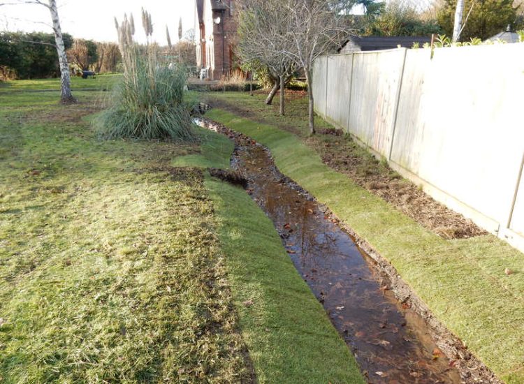 Garden Drainage and Brook Management Worplesdon, Guildford, Surrey - An existing brook had become over grown and blocked with vegetation and silt build up. Brook was cleared, re-ditched, a new under ground pipe installed, surrounding banks and lawns re-turfed and finally construction of a new Oak sleeper bridge to replace the old one. Garden Drainage - MDB Landscapes